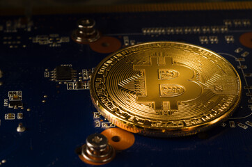 Physical Gold Bitcoin Coin on a computer video card. New independent worldwide cryptocurrency. Bitcoin mining with computer.