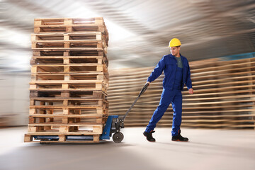 Worker moving wooden pallets with manual forklift in warehouse
