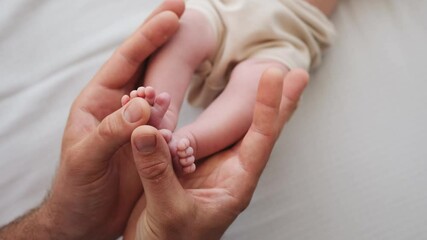 Father holding tiny feet of newborn baby in his hands and petting them. Parent of adorable infant cares about his child at home. Beautiful moments of fatherhood - Powered by Adobe