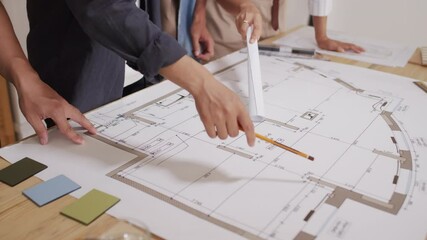 Close up of unrecognizable team of architects working on house blueprint rolled out on desk in their office - Powered by Adobe