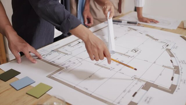 Close up of unrecognizable team of architects working on house blueprint rolled out on desk in their office