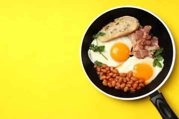 Pan with tasty breakfast on yellow background