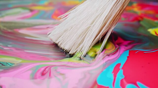 Clean brush spreading multi-colored layer of paint on paper