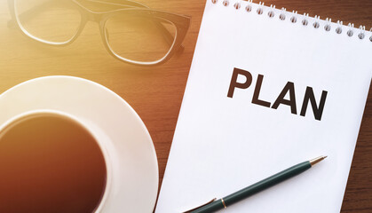 Notebook with text Plan on table with coffee, pen and glasses in sunlight