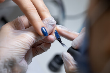 the manicure master holds the client's finger and applies a blue gel polish to the nail