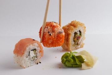 a hand and Chinese chopsticks holds a roll over other sushi, a portion of Asian food, rolls