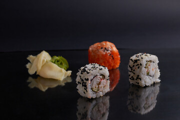 several different rolls on the table, asian food, side view, dark background, sushi, ginger and wasabi