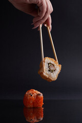 a hand and Chinese chopsticks holds a roll over other sushi, a portion of Asian food, rolls