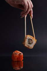 a hand and Chinese chopsticks holds a roll over other sushi, a portion of Asian food, rolls
