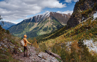 Naklejka na ściany i meble travel to Caucasus mountains in Karachay-Cherkessia, Arkhyz. Man in yellow hipster hoodie hiking in mountains with travel backpack. Wandering lifestyle, adventure concept autumn vacation in wild