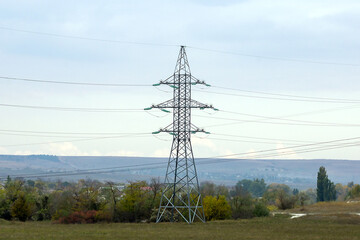 The power line support stands high in the mountains. Photographed in close-up. Electrical wires are connected to the support on both sides.