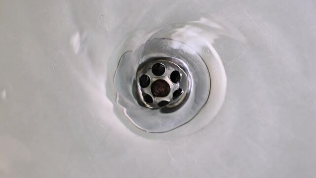 Water swirling down the drain hole of a stainless steel sink, close up
