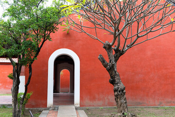 Bright Red wall of Chinese temple with arched door, the old trees beside.