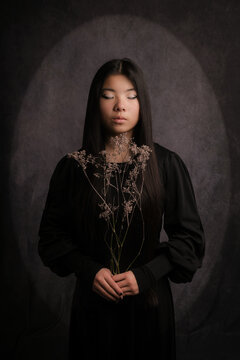 classic dark painterly studio portrait of asian teenager girl in black wearing makeup
