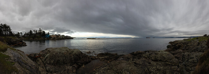 Panoramic View of Rocky Shore on the West Pacific Ocean Coast during cloudy winter evening. Taken at Saxe Point Park, Victoria, Vancouver Island, British Columbia, Canada.