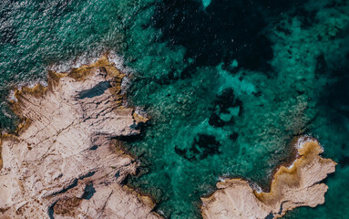 Vertical aerial drone view of the rocky coast and the clear sea of Frioul islands, on a sunny day.