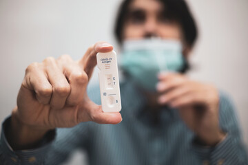 A man holds the positive antigen rapid test kit while inserting the rod into his nose.COVID19,...