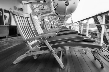 Black and white deckchairs, with blue folded cushions, lined up on a cruise line on a cloudy port day. Liferafts can be seen hanging above the deck. With space for text. - 477633916
