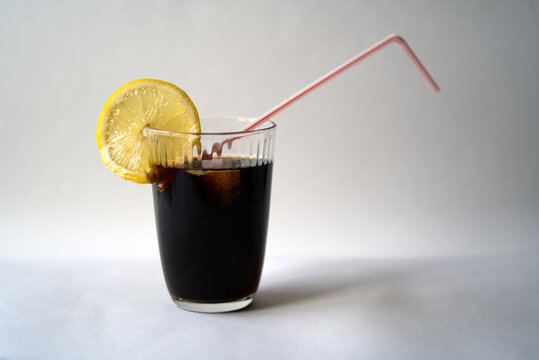Glass of cola with straw, lemon slice and ice cube. Photo taken December 30th, 2021, Zurich, Switzerland.