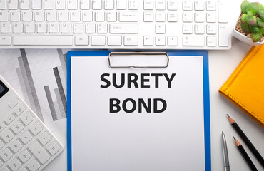 SURETY BOND written on the paper with keyboard, chart, calculator and notebook