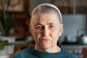 An old woman with deep wrinkles and gray hair looks at the camera. There is a headband on the head....
