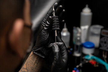 Fototapeta na wymiar Tattooist assembling the sterilized needle in the grip. Wearing black gloves. Body art concept
