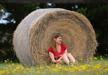 Naklejka na ściany i meble Female sitting next to hay bale.