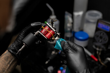 Tattooist setting up and adjusting his tattoo machine. Wearing black gloves. Body art concept