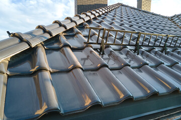 Closeup snow guard for safety in winter on house roof top covered with ceramic shingles. Tiled covering of building