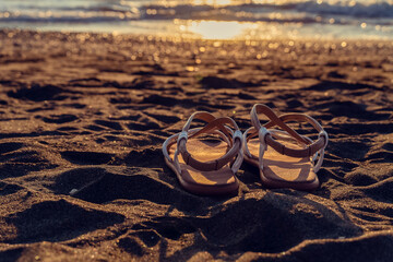 Leather sandals lie on the sand on the beach near the sea at sunset with copy space. Beautiful background on the theme of travel, beach holidays