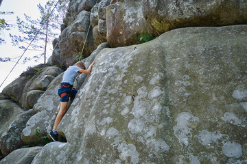 Young child boy climbing steep wall of rocky mountain. Kid climber overcomes challenging route. Engaging in extreme sport concept