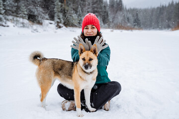 cheerful girl in bright clothes sits with her dog in the snow. Portrait of the dog and its owner. A red-haired little dog.