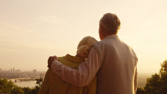 Aged man and woman hugging at sunset on rooftop, romantic date in retirement