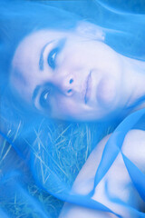 young woman lying in the grass with blue transparent cloth covering her