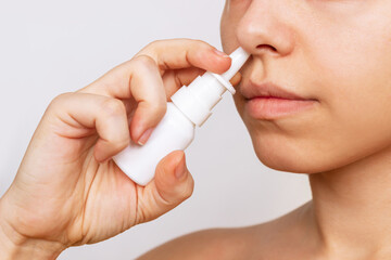Cropped shot of a young caucasian woman using nasal spray for a runny nose and congestion isolated on a white background. Treatment of the disease. Rhinitis, sinusitis, cold. Dependence on drops - obrazy, fototapety, plakaty