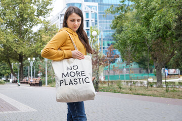 A woman shows a fabric reusable bag with the text no more plastic.