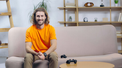 KYIV, UKRAINE - DECEMBER 22, 2021: cheerful man looking at camera while sitting on couch near joysticks.