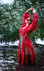 woman in red dress and masquerade standing in water and looking to sky