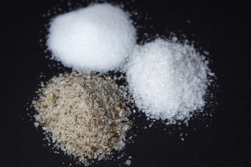 Different types of salt on a black background. Fine salt and salt with spices.