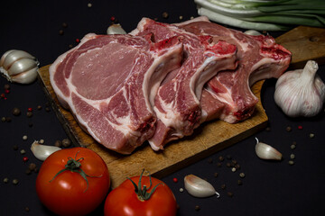 Pork meat on a black background. Meat loin with bone on a wooden board. Meat cooking