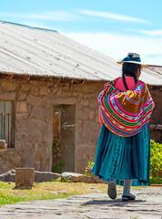 Unrecognizable indigenous Peruvian Quechua woman in traditional clothing walking in a street of Taquile Island by the Titicaca Lake, Peru.