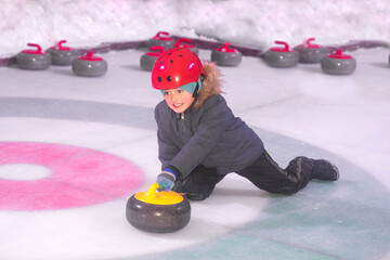 
boy on ice plays curling sport game. child pushing a sports equipment stone