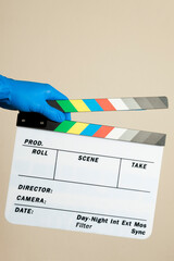 Hand in blue surgical glove hitting a movie clapperboard on neutral background. Film set with security protocol against covid 19. Clapperboard concept. concept of safety at work.
