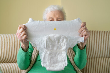 wrinkled hands of a senior woman or man holding white adult diaper pad