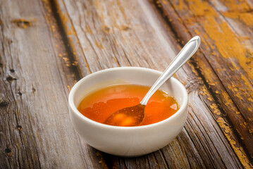 Bee honey and spoon in white bowl over wooden table.