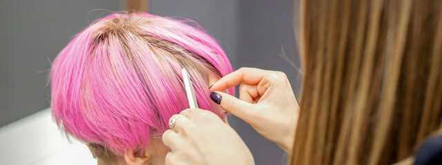 Fototapeta premium Hairdresser prepares dyed short pink hair of a young woman to procedures in a beauty salon