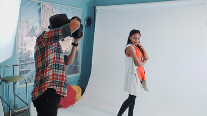 Behind the scenes on photo shoot: professional photographer working in studio by taking photos of black model. Photo shoot for stylish fashion magazine.