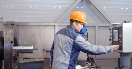 Portrait of a young worker in a helmet at a large metalworking plant. An engineer maintains machines and manufactures parts for petroleum equipment.