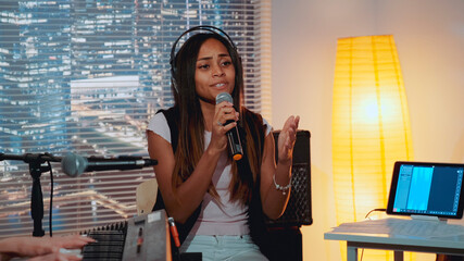 Home recording studio: multiracial pretty vocalist singing song into microphone while her female...