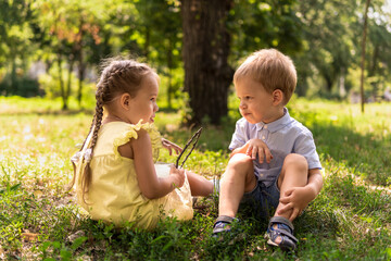 Two happy smiling cheerful toddler preschool twins siblings children brother sister boy girl communicate talk together on grass lawn in park in sunny hot summer. childhood, friendship, family concept